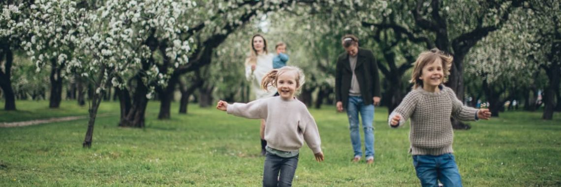 A happy family running and playing among blooming trees in a lush green park during spring.